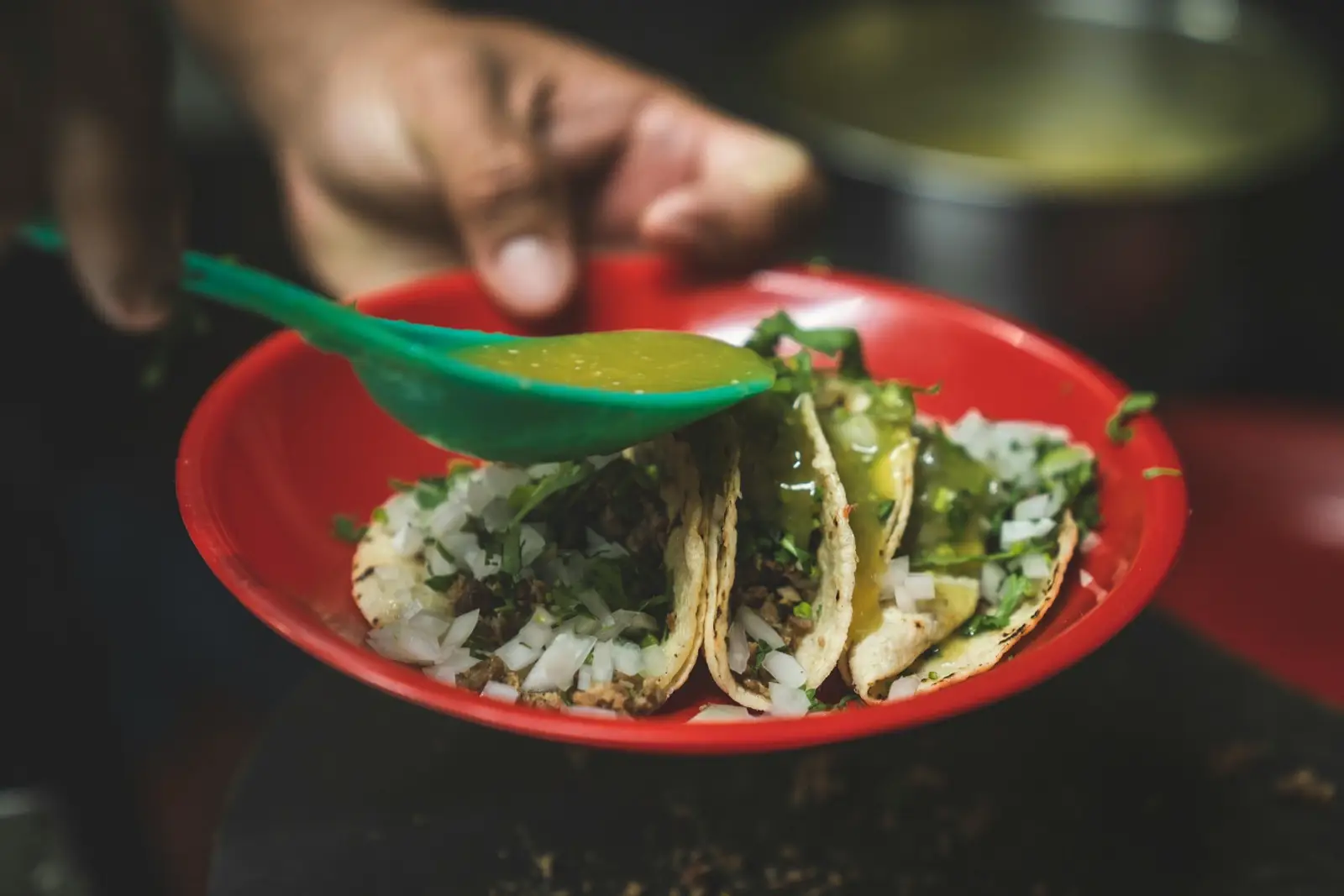 Authentic street tacos topped with cilantro and onion in a red bowl, drizzled with green salsa