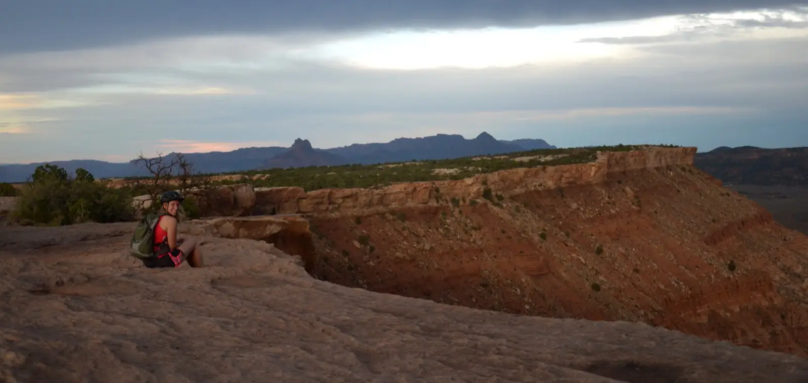 A rider rests on the South Rim slickrock of Gooseberry Mesa with the Zion peaks silhouetted in the distance