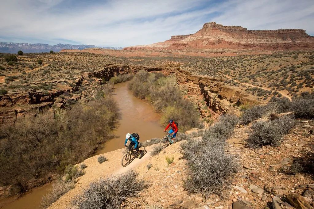 Mountain bikers on singletrack above the Virgin River corridor with red rock mesas in the distance