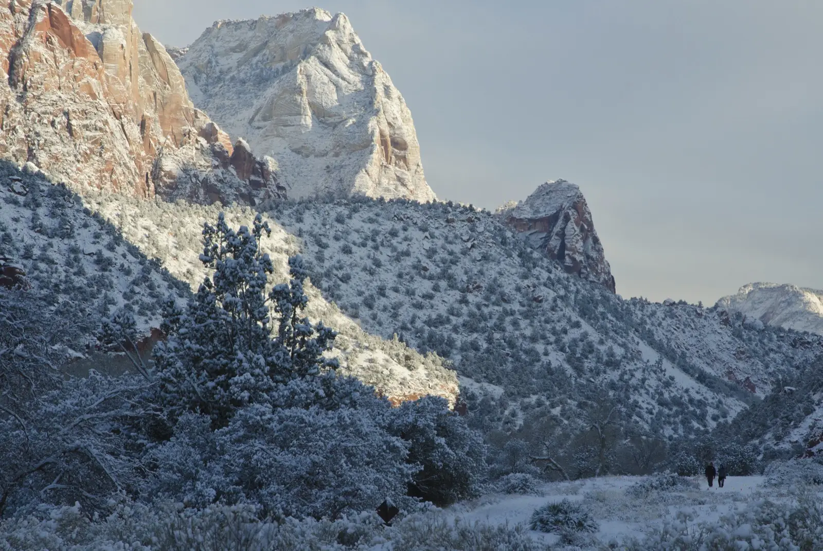 Walkers on the snowy Pa'rus Trail with the dramatic peaks of Zion's lower canyon rising above