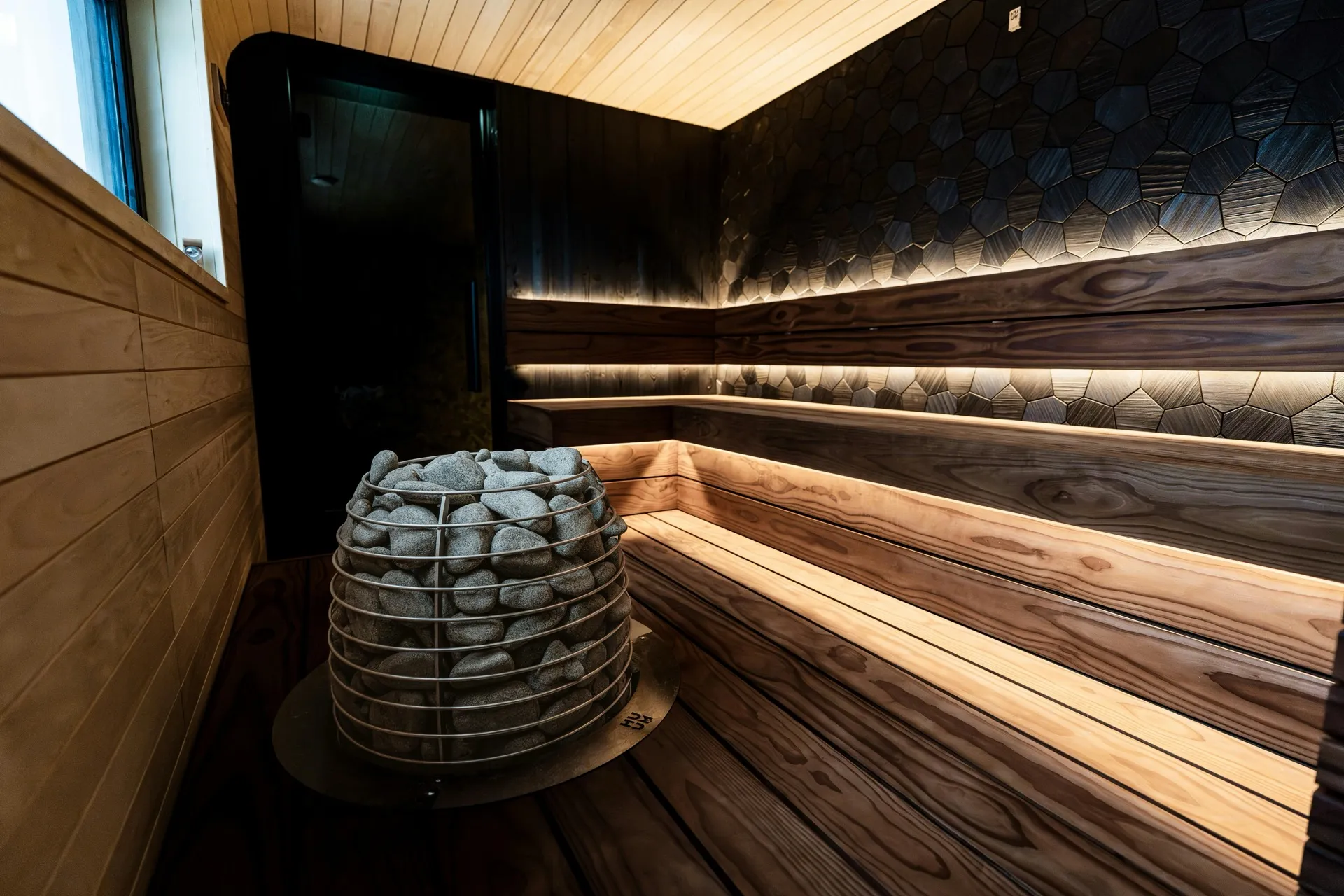 Luxury sauna interior with warm wood benches, stone heater, and ambient backlighting