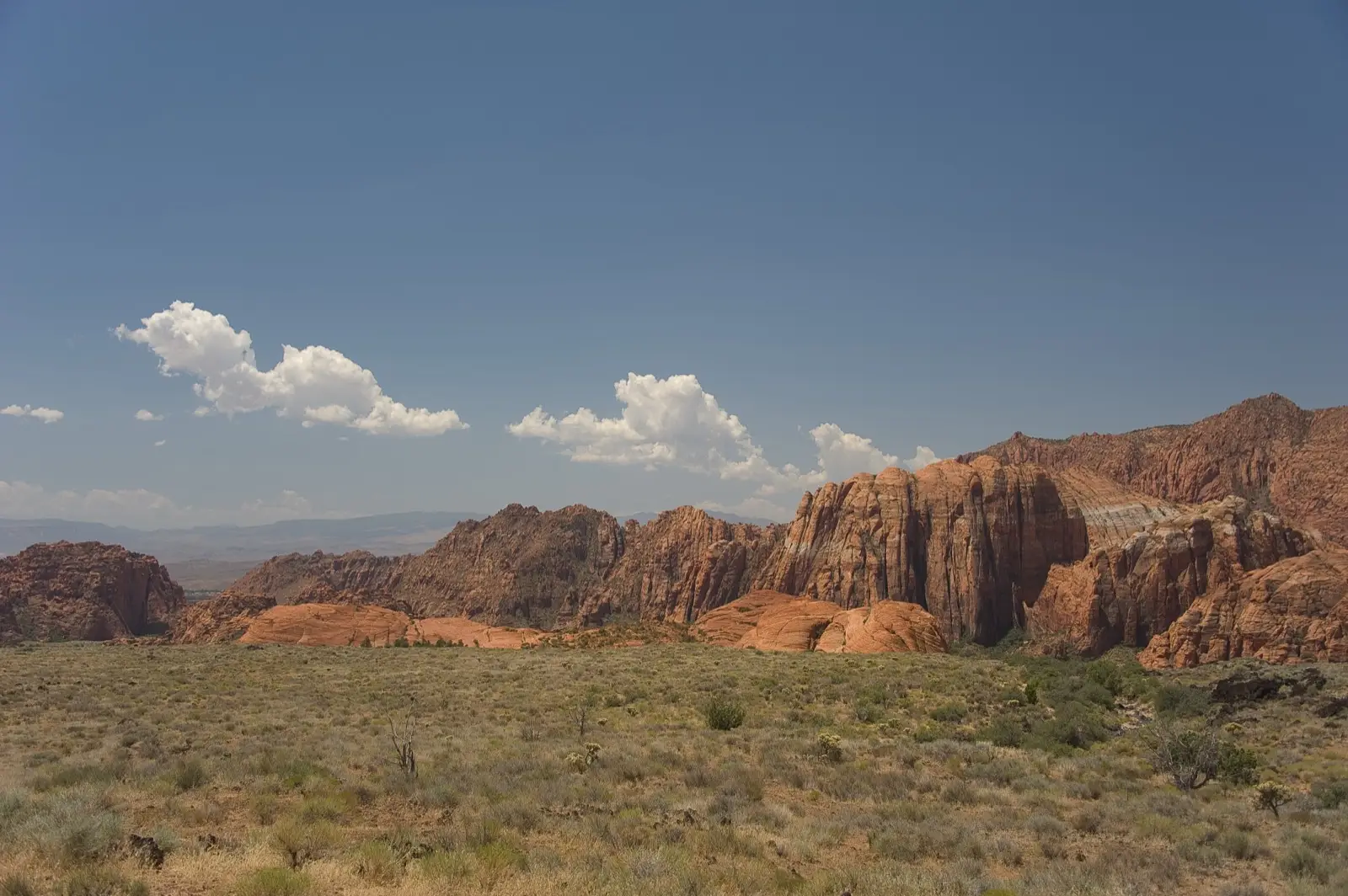 Red Navajo sandstone cliffs of Snow Canyon State Park rising above grassland under a desert sky