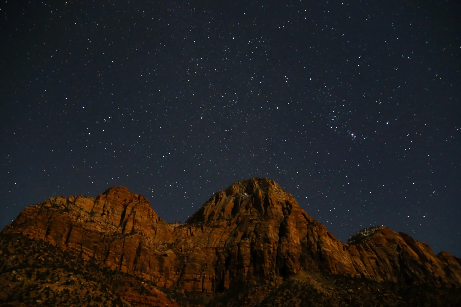 Stars and the constellation Orion above the moonlit red cliffs of Bridge Mountain in Zion National Park