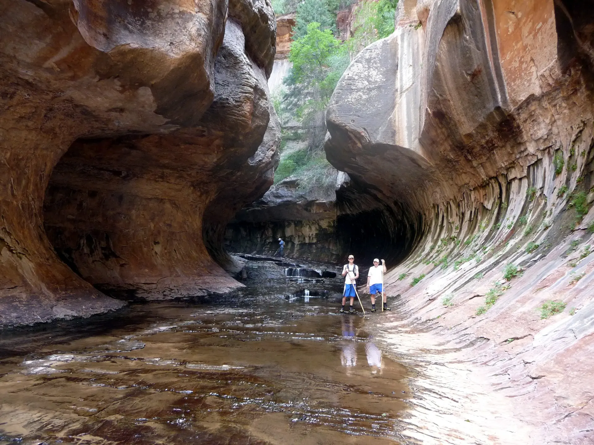 Hikers inside the iconic tube-shaped sandstone formation of The Subway in Zion's Left Fork, with reflected pools below