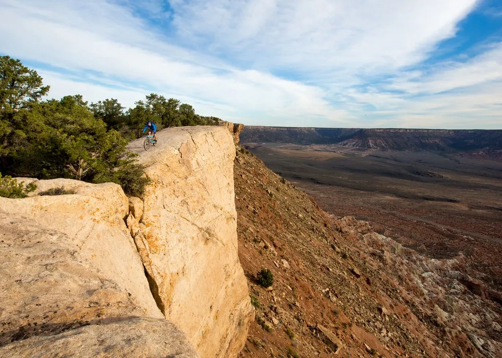 Mountain biker on slickrock at the edge of a mesa rim above a vast desert valley