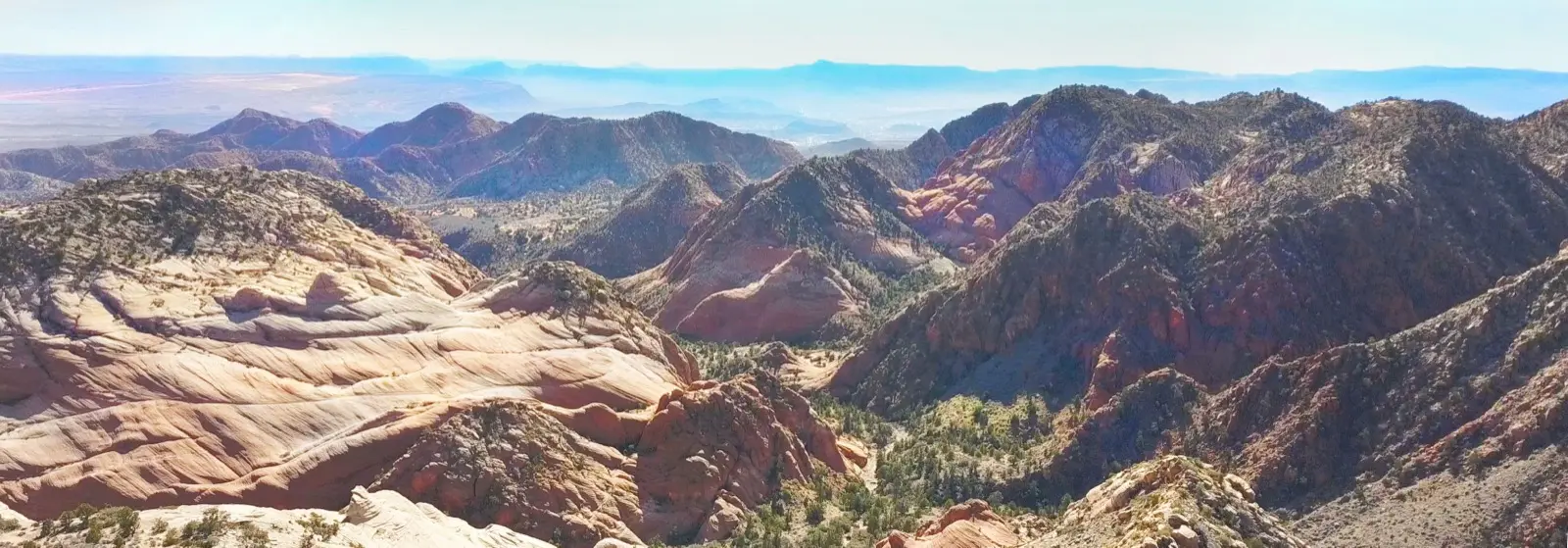 Panoramic view of the Candy Cliffs at Yant Flat — pink, white and orange striated sandstone ridges spreading toward distant hazy peaks