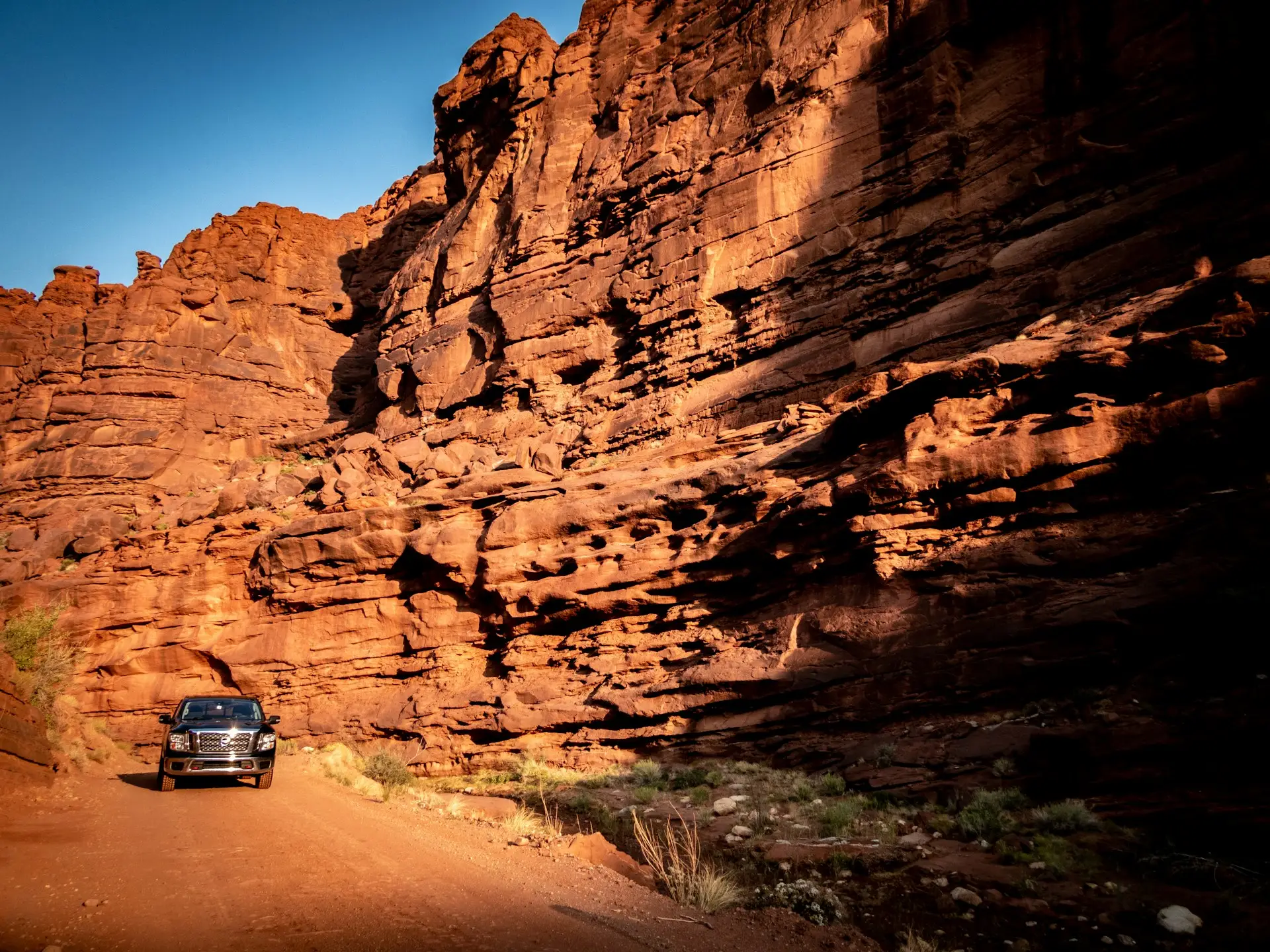A 4x4 vehicle on a backcountry dirt road below towering red sandstone cliffs in southern Utah