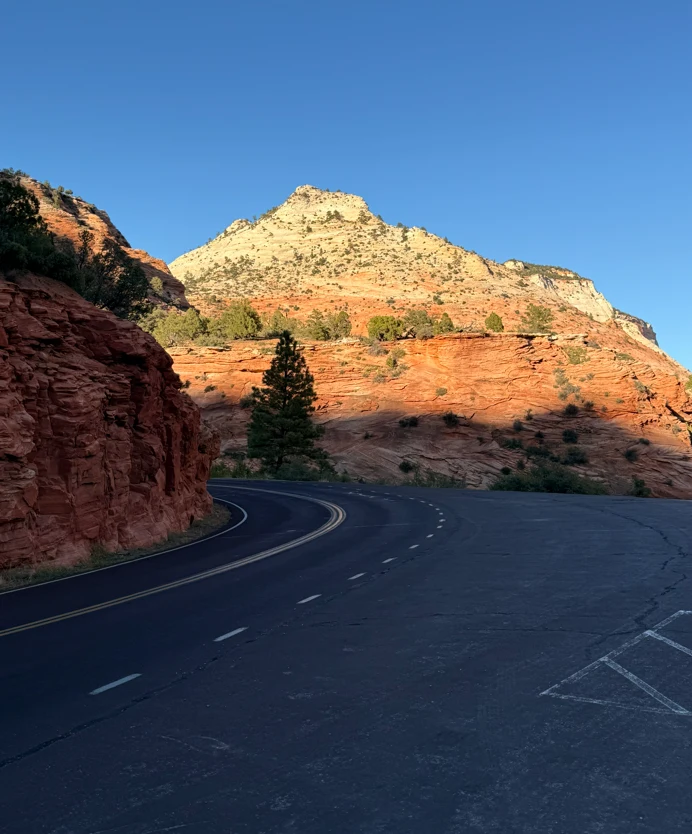 Paved road curving beneath a red and white sandstone mountain in Southern Utah