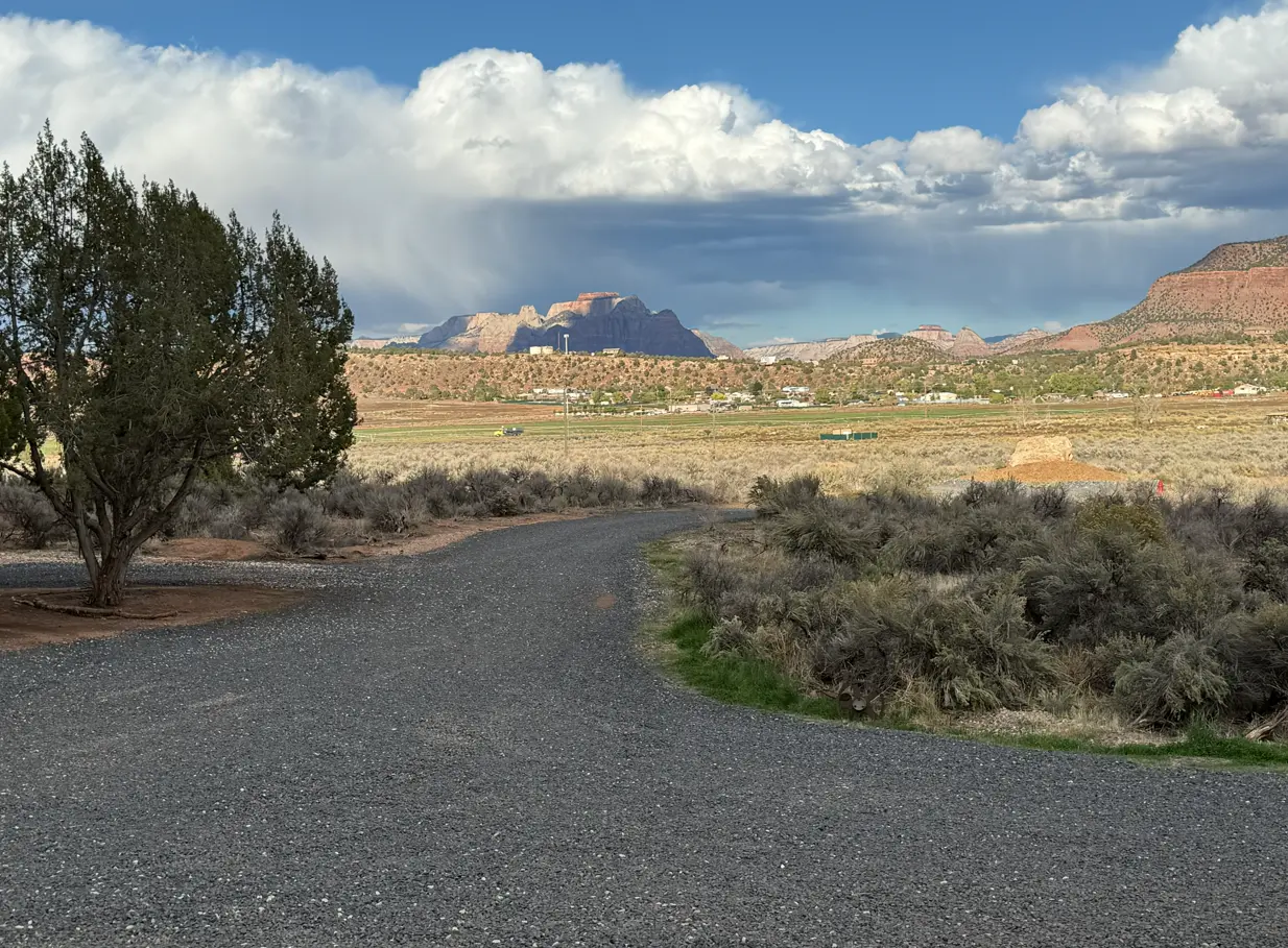 Gravel road running through sagebrush toward distant mesas under a cloudy sky